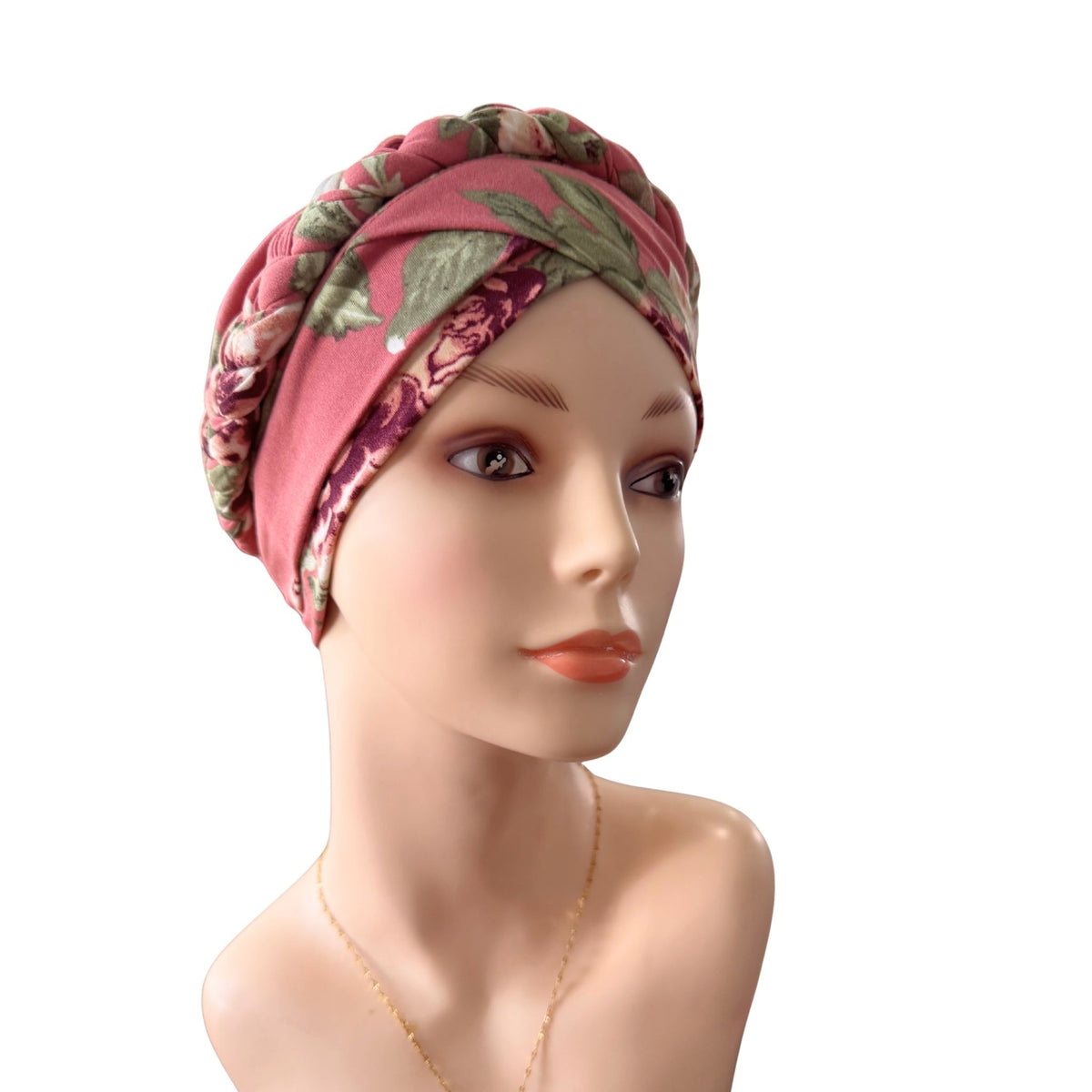 A pink floral headwrap turban hat with green leaves, displayed on a female mannequin bust against a solid white background.