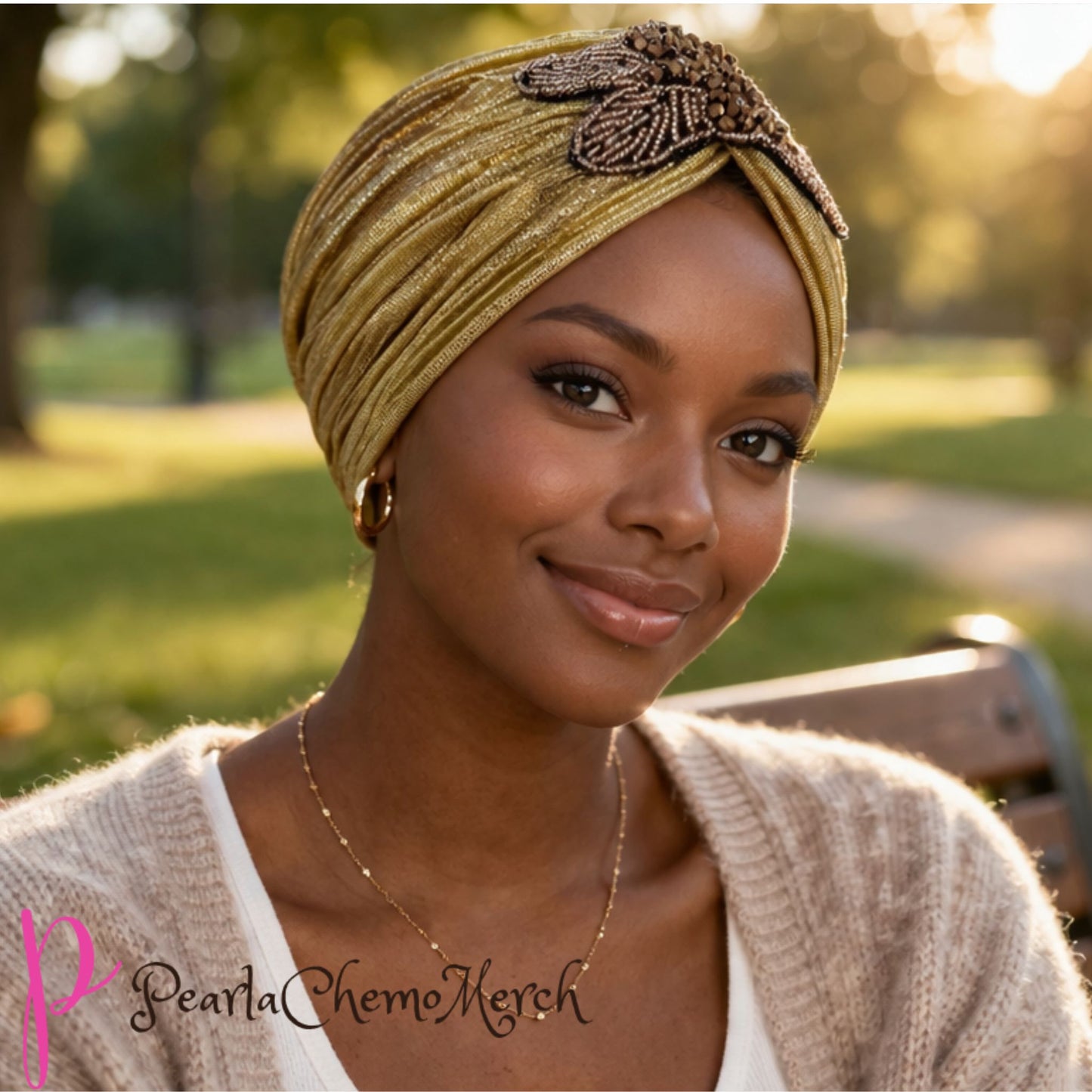 Woman wearing a gold chemo turban with a decorative leaf in a park setting, with 'Pearl of Chemo Merck' branding.