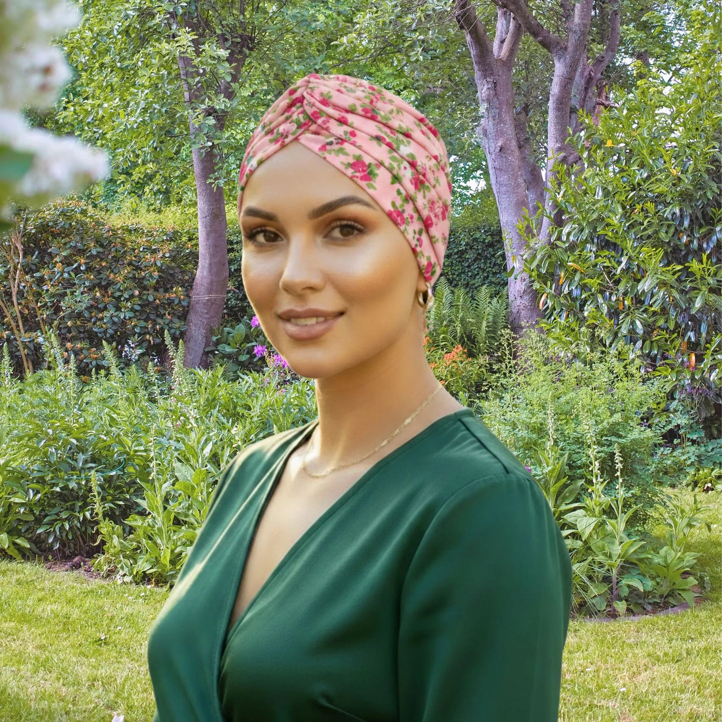 Woman wearing a floral headscarf and green dress in a garden setting